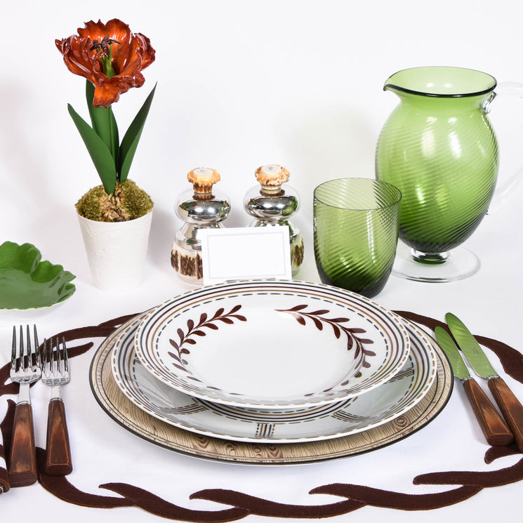 Dining table setting with decorative plates, glasses, and cutlery on a white background